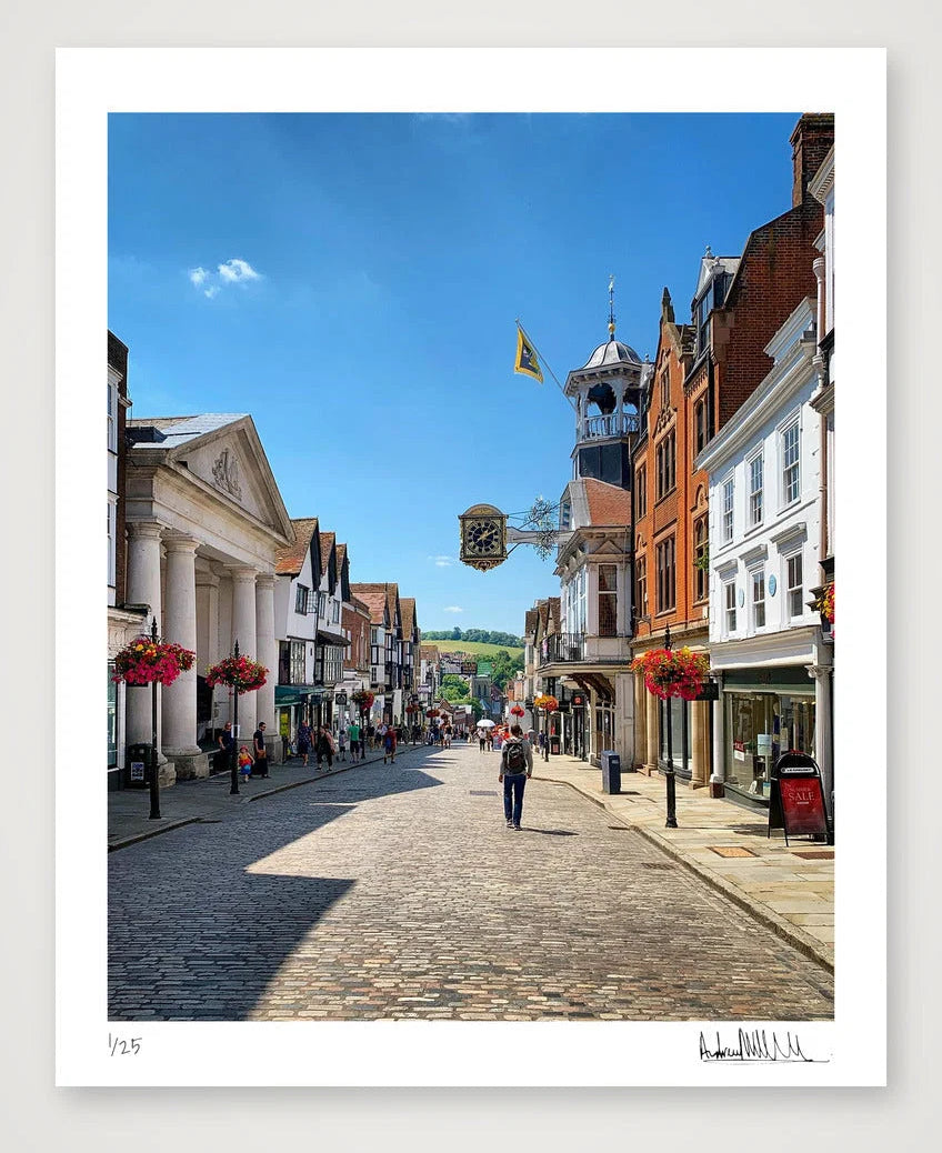 A distant view along Guildford's historic High Street with Tunsgate to the left, the Guildhall to the right and in the far distance the green hills and woods of The Mount.